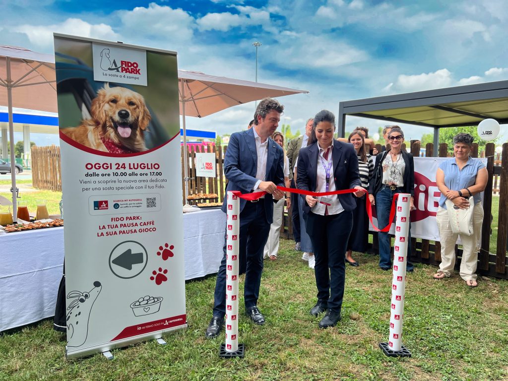 Due tagliano un nastro rosso al Fido Park mentre altri guardano.