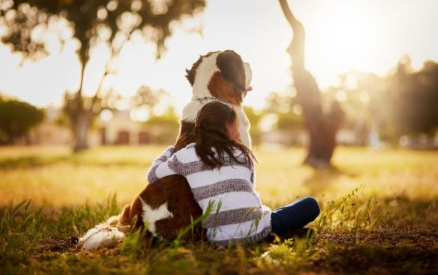 Una ragazza abbraccia un cane nel parco, a simboleggiare la cura nella giornata contro l'abbandono.