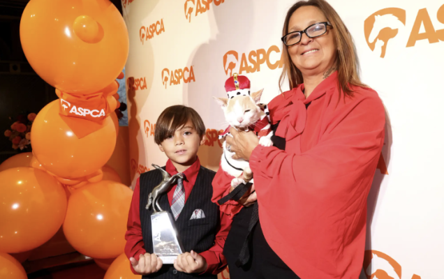Donna con gatto in costume e ragazzo con trofeo a un evento ASPCA.