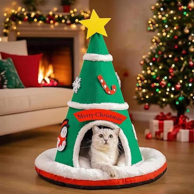 Gatto che si riposa in una casa festosa a forma di albero vicino a un albero di Natale illuminato.